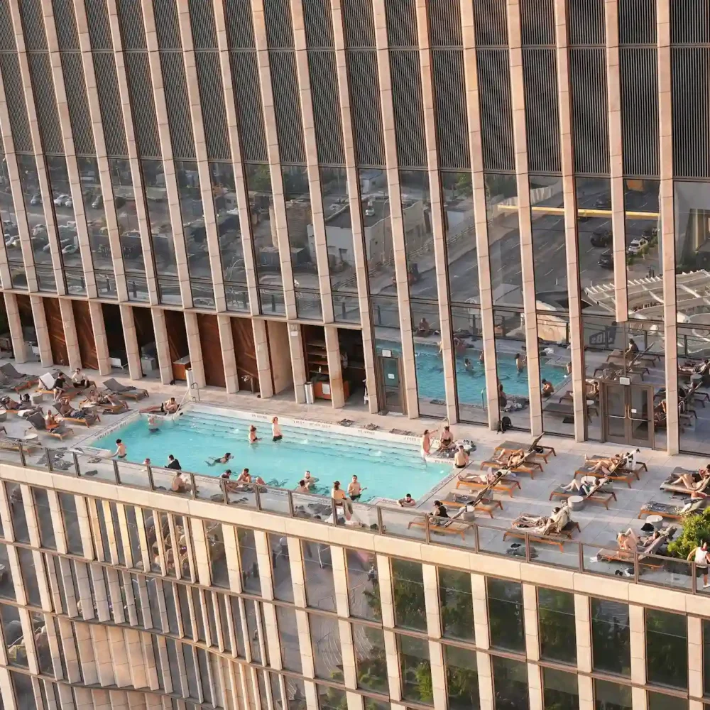 Rooftop pool atop modern high-rise, with guests lounging and swimming against panoramic city views and sleek architectural backdrop