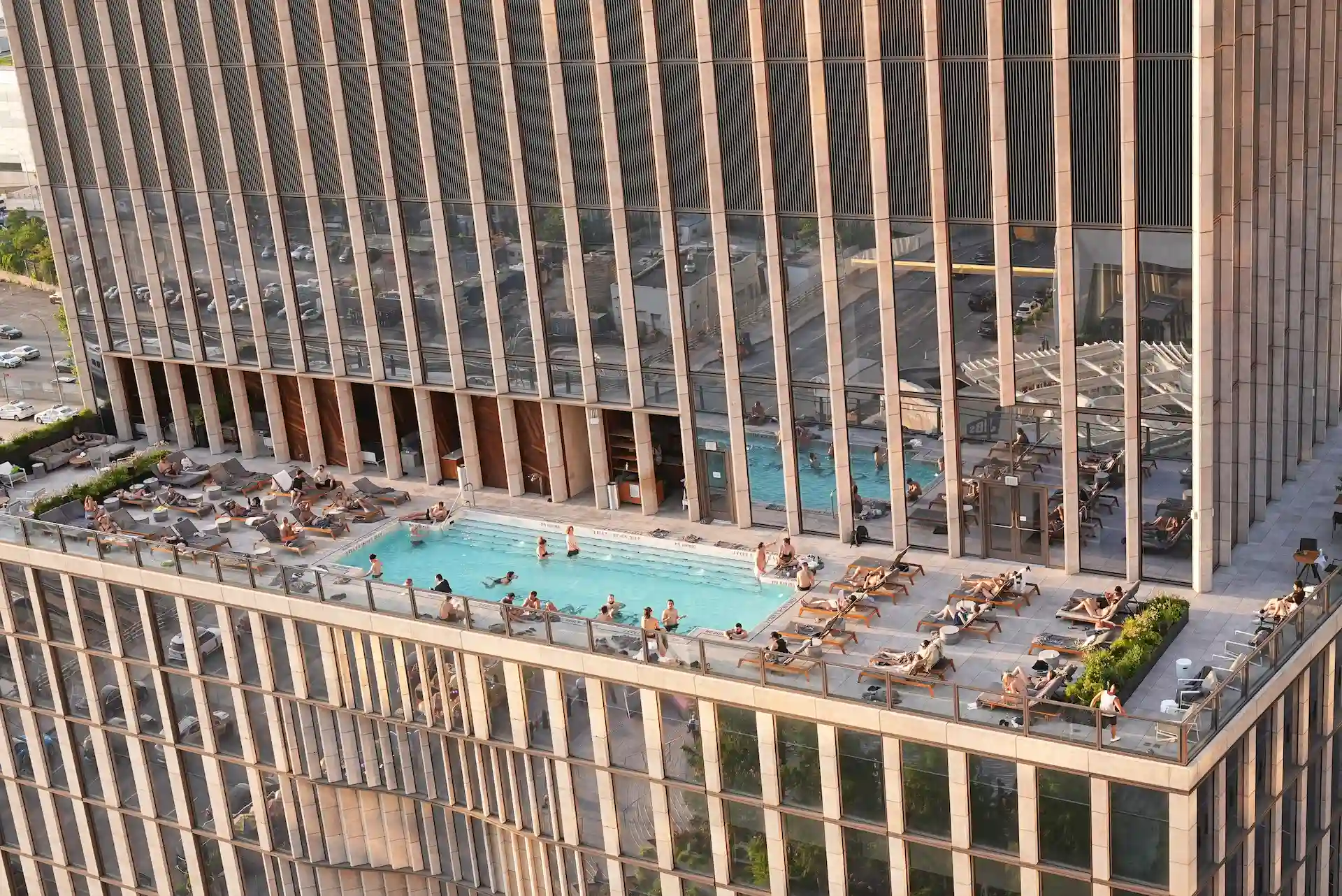 Rooftop pool atop modern high-rise, with guests lounging and swimming against panoramic city views and sleek architectural backdrop