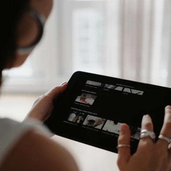 Person holding tablet with video thumbnails on screen, in softly lit room with sheer curtains and calm atmosphere
