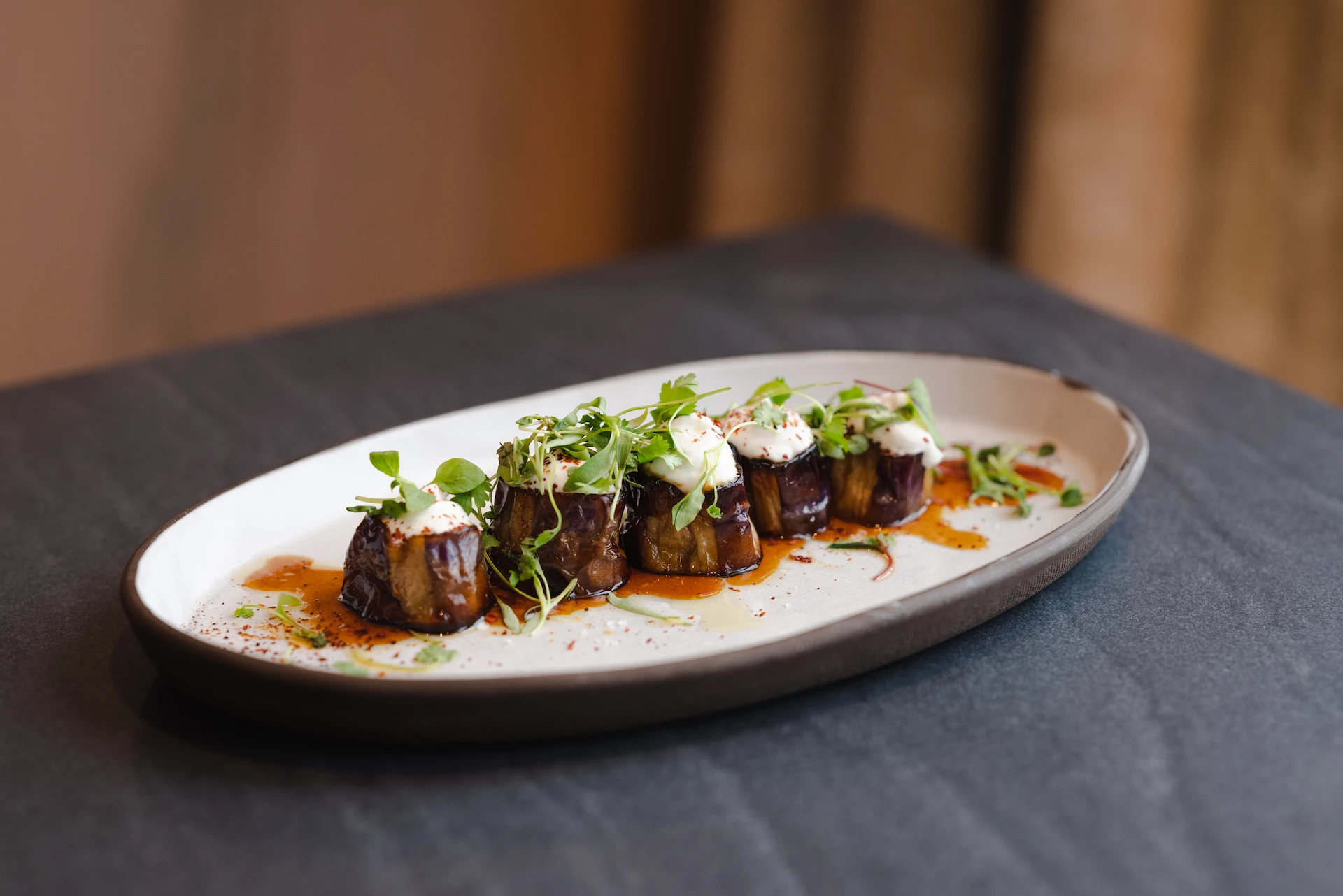 Oval plate of bite-sized delicacies topped with vibrant sauce and fresh microgreens, artfully arranged on a dark tablecloth to create an elegant, sensory dining experience.