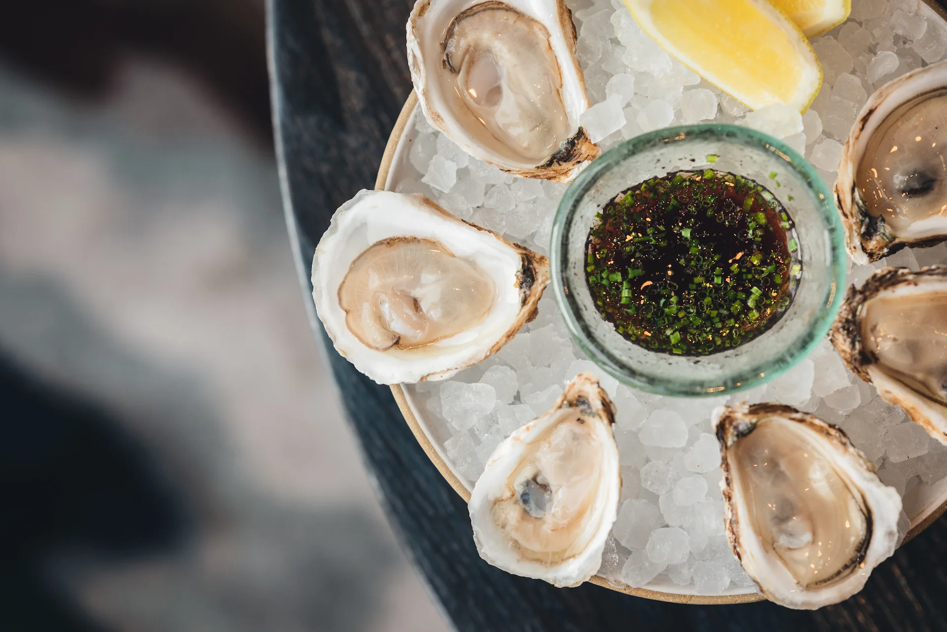 Elegant plate of fresh oysters on crushed ice with lemon wedges and herb-topped sauce, evoking refined coastal indulgence