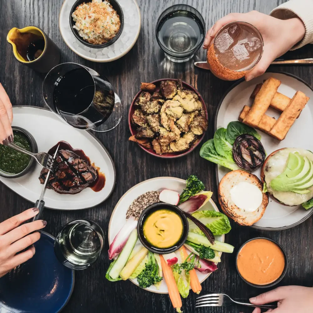 Top-down view of a shared dining table adorned with colorful, artfully plated dishes and drinks, with two people enjoying a vibrant meal that evokes connection, warmth, and a lively culinary experience.