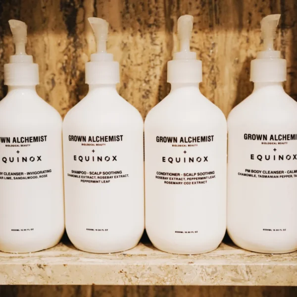 Four white Grown Alchemist bottles co-branded with Equinox, neatly arranged on a wooden shelf in a luxury wellness setting