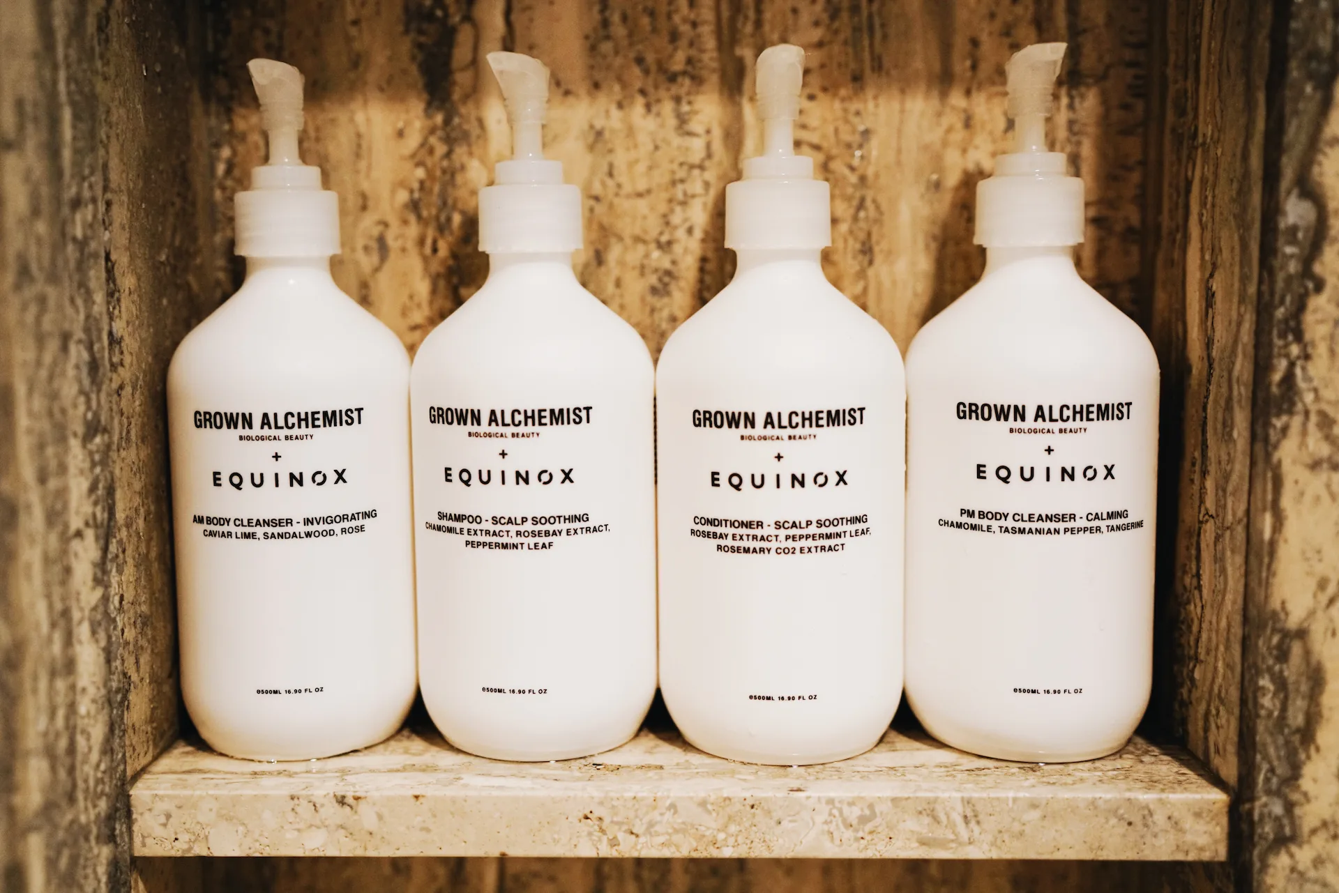 Four white Grown Alchemist bottles co-branded with Equinox, neatly arranged on a wooden shelf in a luxury wellness setting