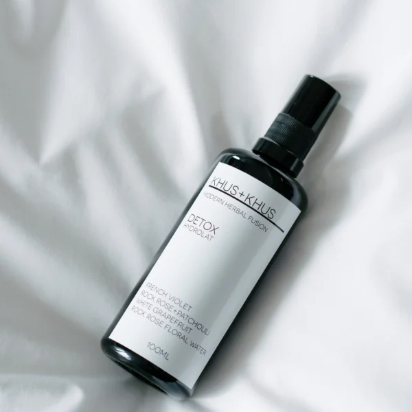Black spray bottle labeled “Detox Hydrolat” resting on white fabric, highlighting botanical ingredients and minimalist design
