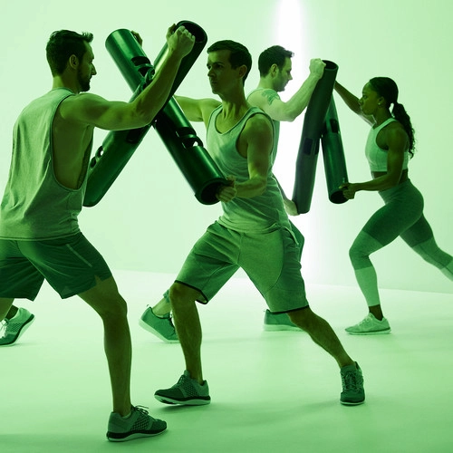 Four individuals doing partner resistance exercises with ViPR tubes in green-lit room, emphasizing functional strength and coordination