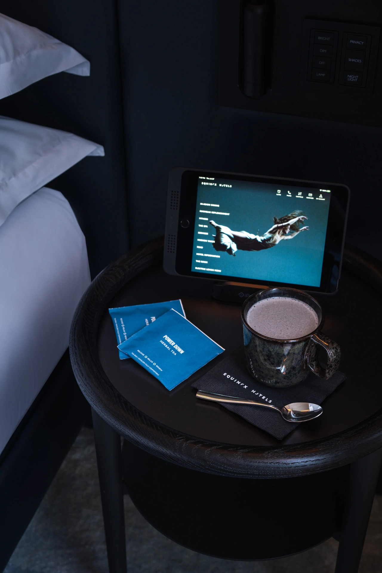 Round black bedside table with tablet showing dinosaur skeletal diagram, coffee mug, spoon, and Square Mile Coffee packets.