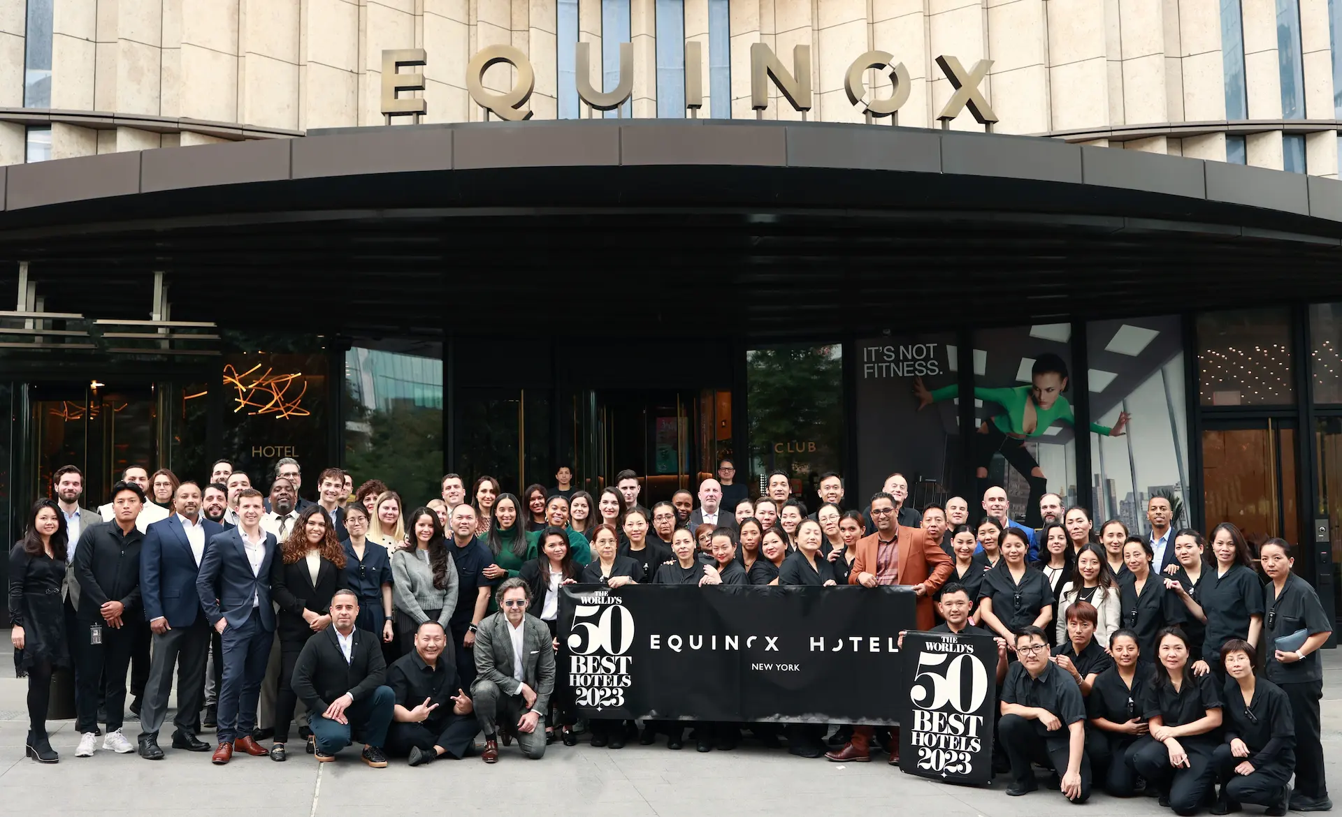 Equinox Hotel New York team celebrating their 50 Best Hotels 2023 award at the hotel entrance, with branded banners and the iconic NYC skyline in the background, capturing a moment of prestige, achievement, and urban luxury.