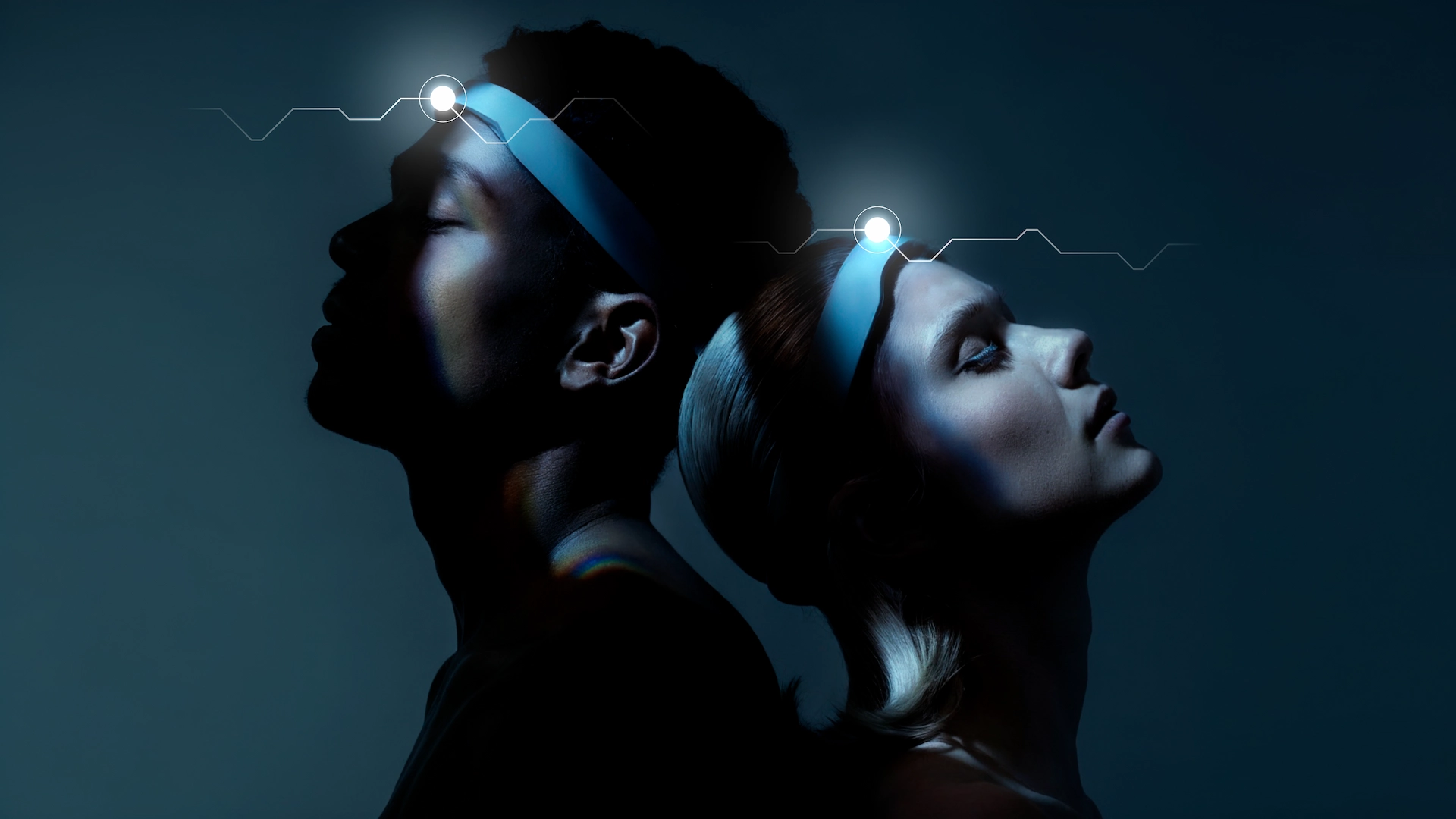 Two people standing back-to-back in dark blue-lit setting, glowing forehead lights with neural graphic above suggesting mental synchronization