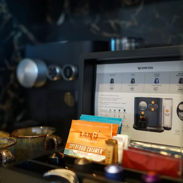 Close-up of Nespresso coffee station with pods, mugs, and creamer packet on dark marble surface