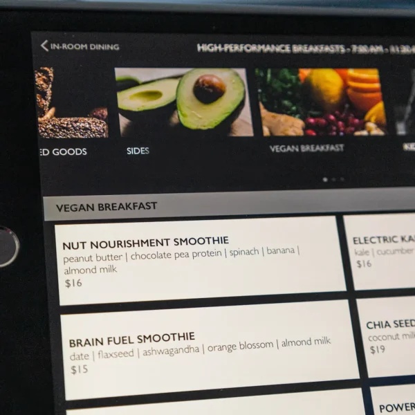 Digital menu screen displaying vegan breakfast options like smoothies and chia bowl, framed by clean layout and wellness-focused language