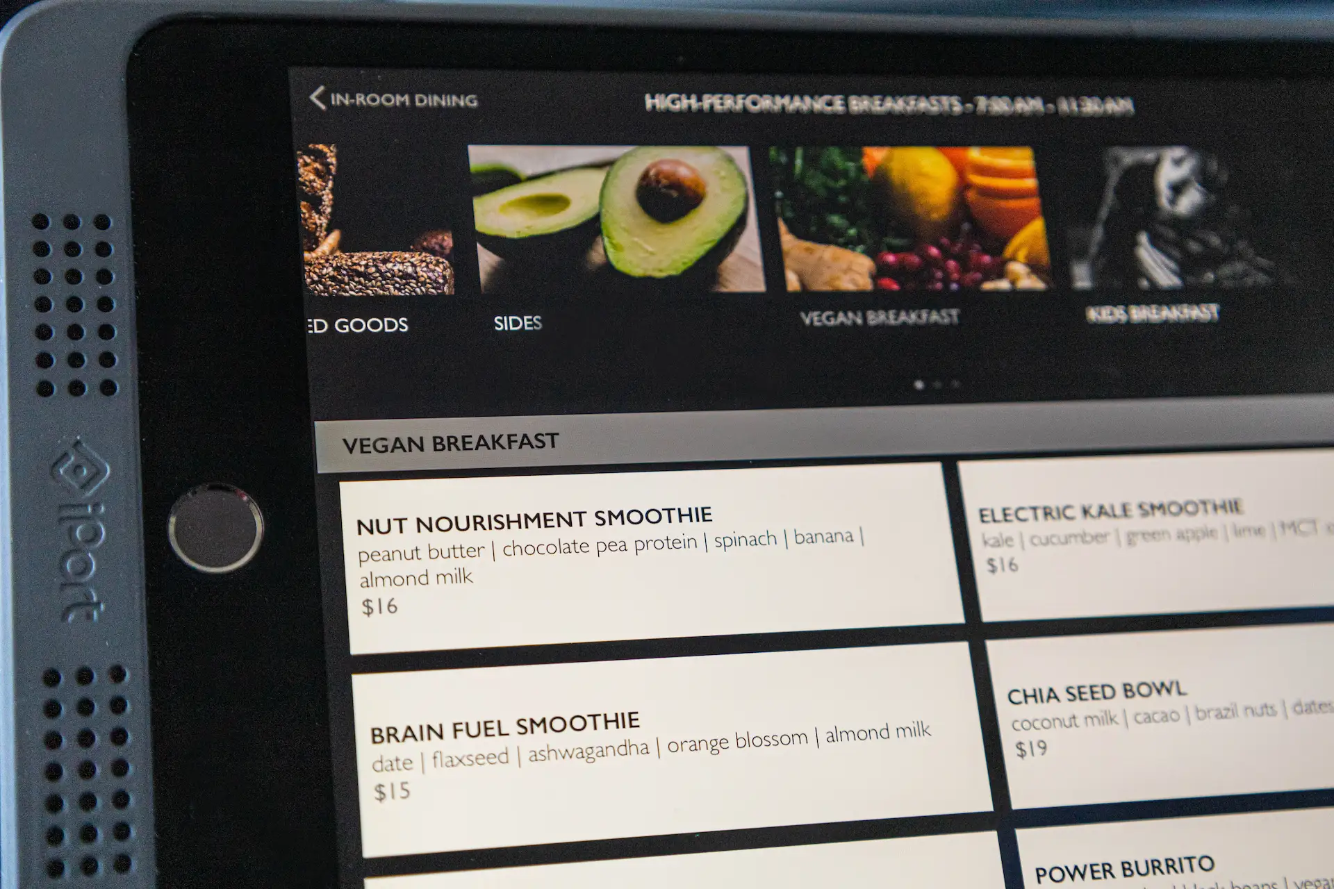 Digital menu screen displaying vegan breakfast options like smoothies and chia bowl, framed by clean layout and wellness-focused language