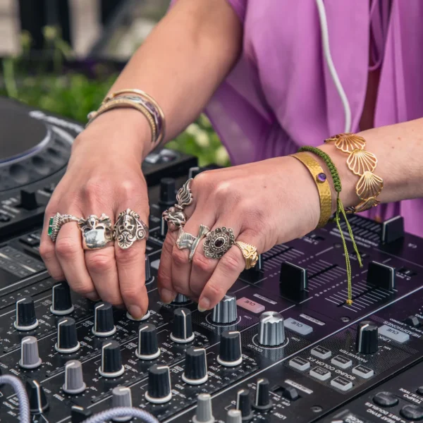 Close-up of hands adjusting DJ mixer knobs, adorned with ornate rings and bracelets, evoking tactile artistry and sonic focus