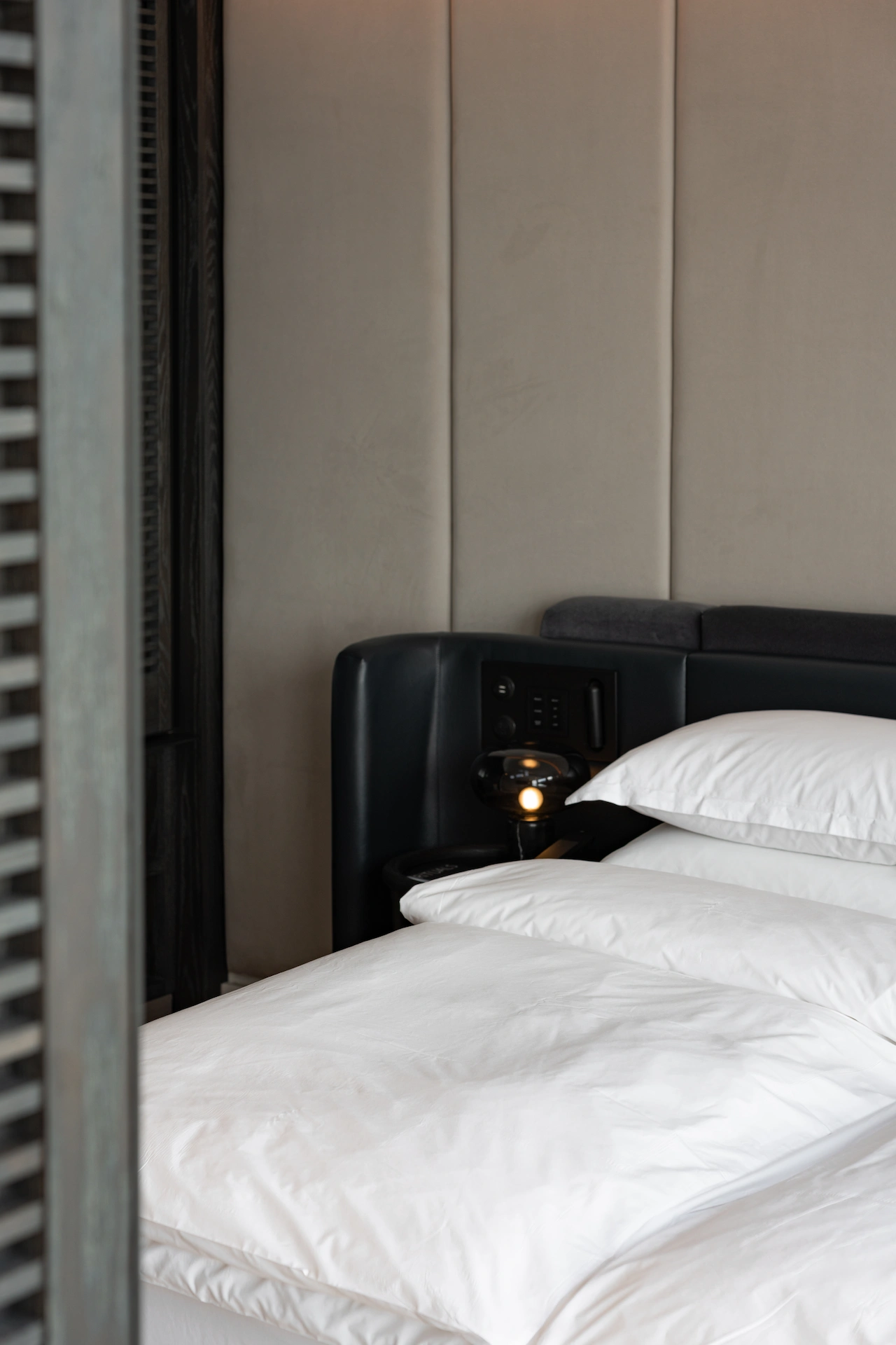 White bed with dark upholstered headboard at Equinox Hotel, light padded wall panels, built‑in lighting and modern design.