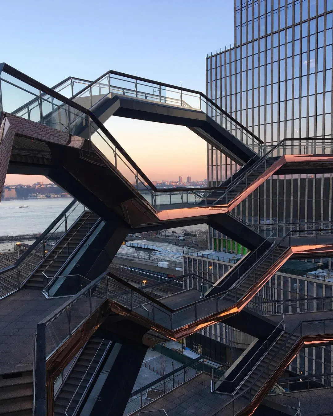 Close-up of the Vessel’s honeycomb staircases at sunset, warm light highlighting geometric design and NYC skyline beyond