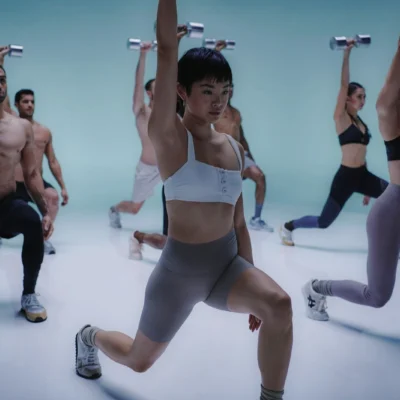 Group fitness session at Equinox Hotel New York, with participants performing lunges holding raised dumbbells in a vibrant blue‑lit studio, showcasing synchronized strength training and high‑energy wellness culture.