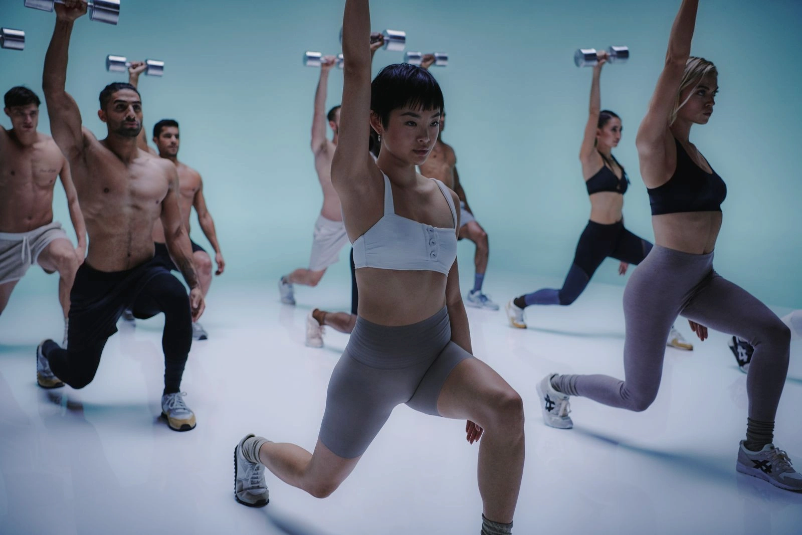 Group fitness session at Equinox Hotel New York, with participants performing lunges holding raised dumbbells in a vibrant blue‑lit studio, showcasing synchronized strength training and high‑energy wellness culture.