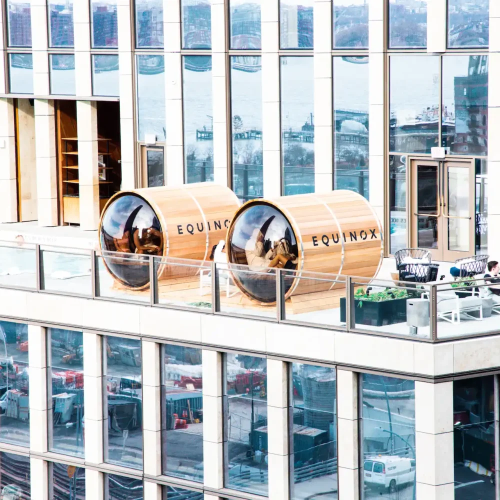 Equinox rooftop with wooden sauna pods, lounge chairs, and cityscape views over water, blending architecture and relaxation