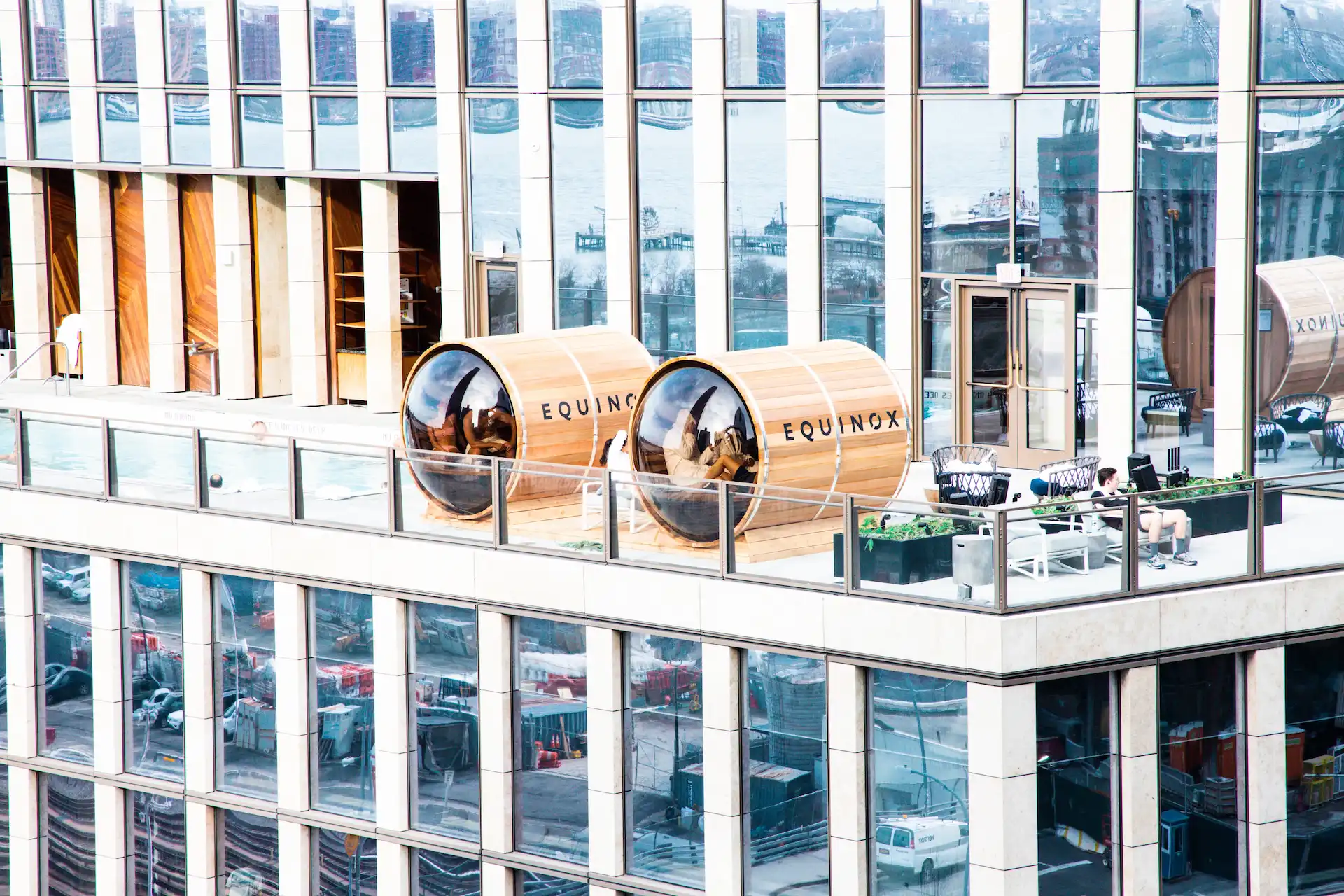 Equinox rooftop with wooden sauna pods, lounge chairs, and cityscape views over water, blending architecture and relaxation