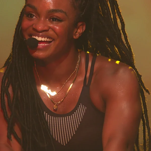 Smiling person in mesh sports bra and headset, glistening with sweat in warmly lit setting, evoking energy and connection