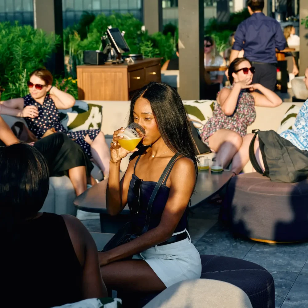 People enjoying drinks at outdoor lounge with plants and city views, evoking relaxed social vibe