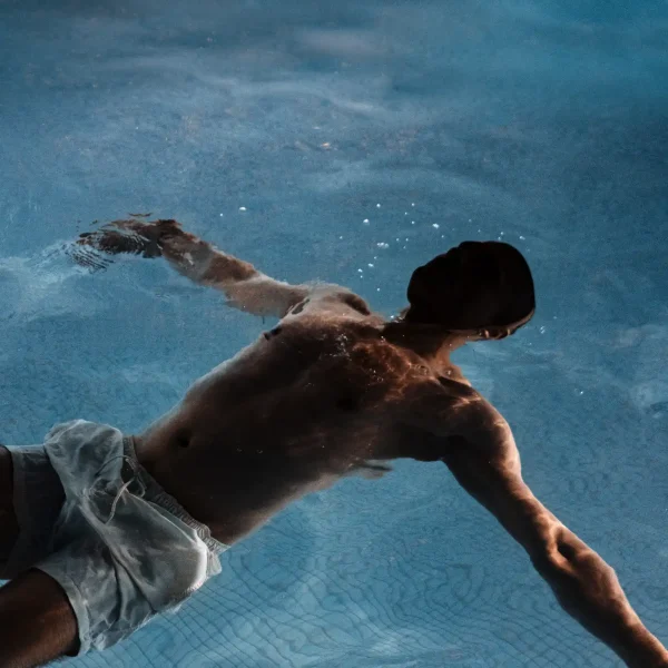 Man floating calmly in pool, surrounded by soft ripples and natural light, evoking quiet recovery and aquatic stillness