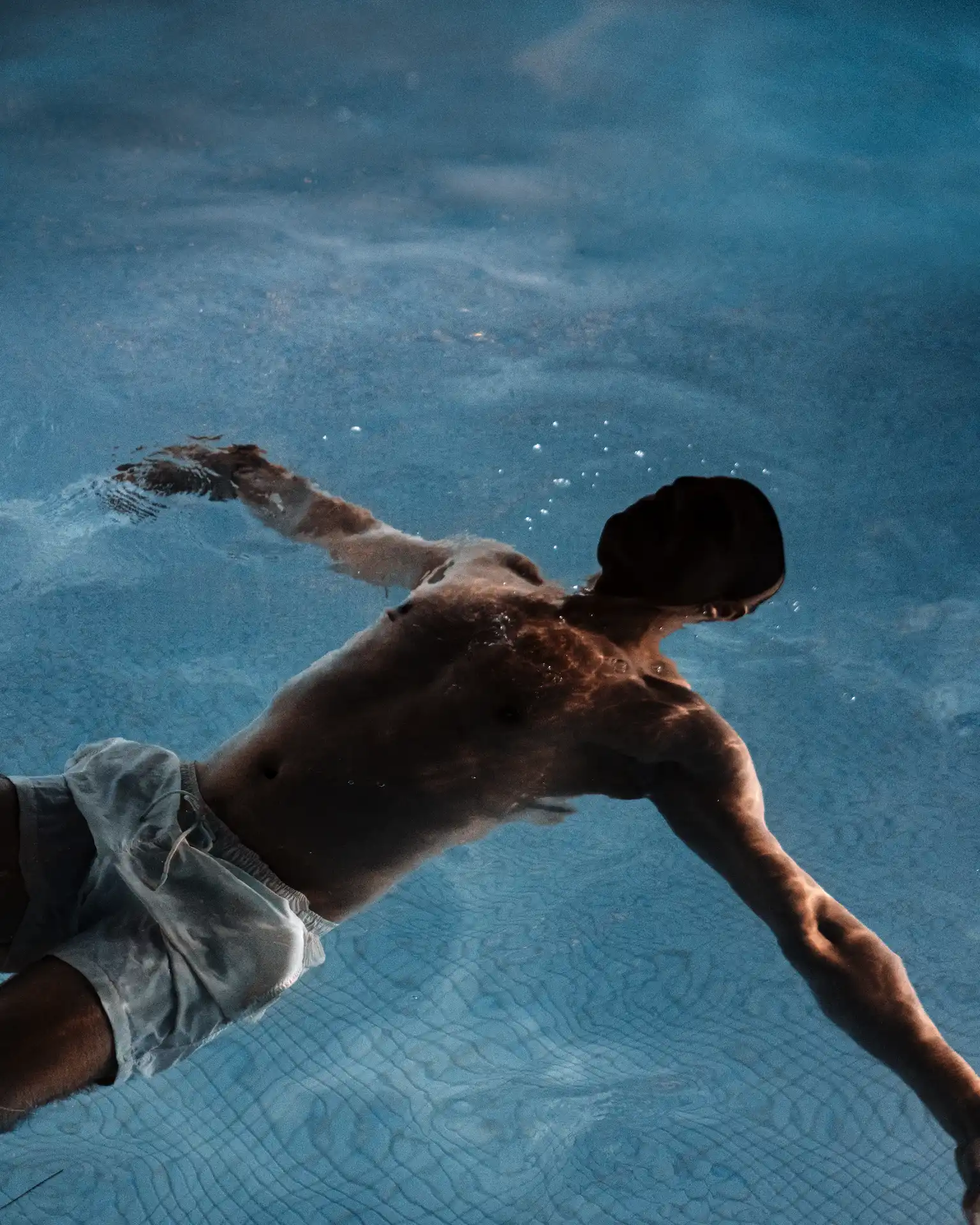 Man floating calmly in pool, surrounded by soft ripples and natural light, evoking quiet recovery and aquatic stillness