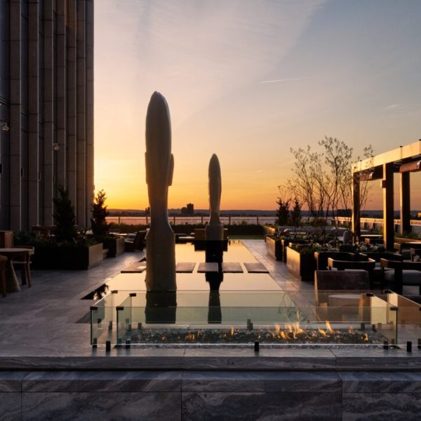 Rooftop terrace at sunset with sculptures, fire pit, seating and water views in elegant urban setting