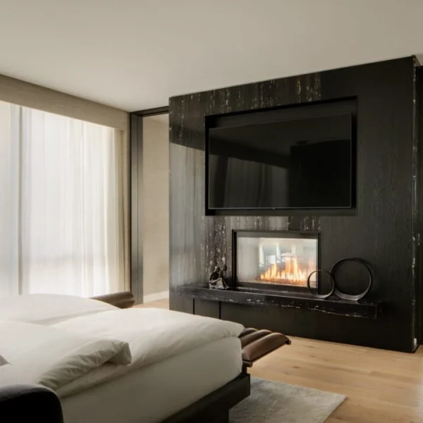 Modern bedroom with fireplace, TV, white bedding and sculptural decor in sunlit minimalist interior