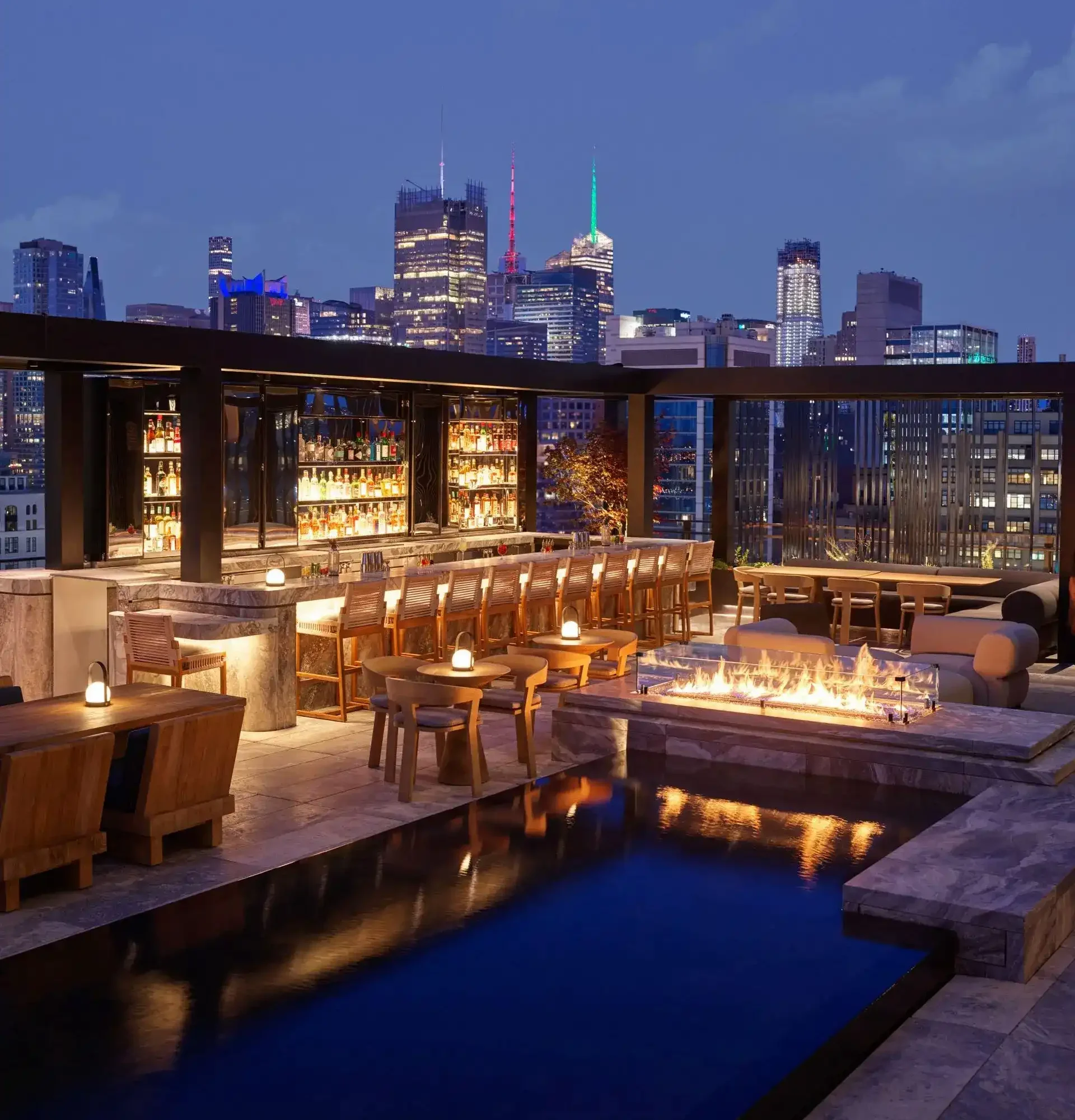 Rooftop bar at night with pool, fire pit, and city skyline, evoking vibrant urban luxury
