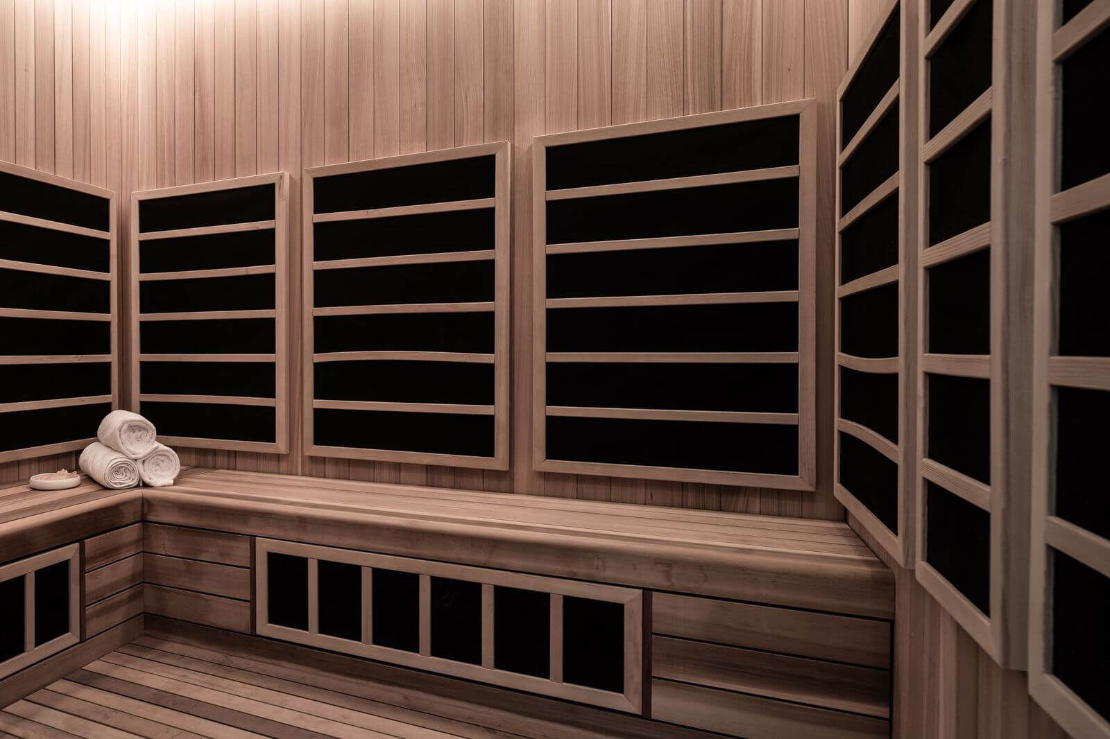 Interior of modern infrared sauna with light wood panels, heating slats, and rolled white towels on bench