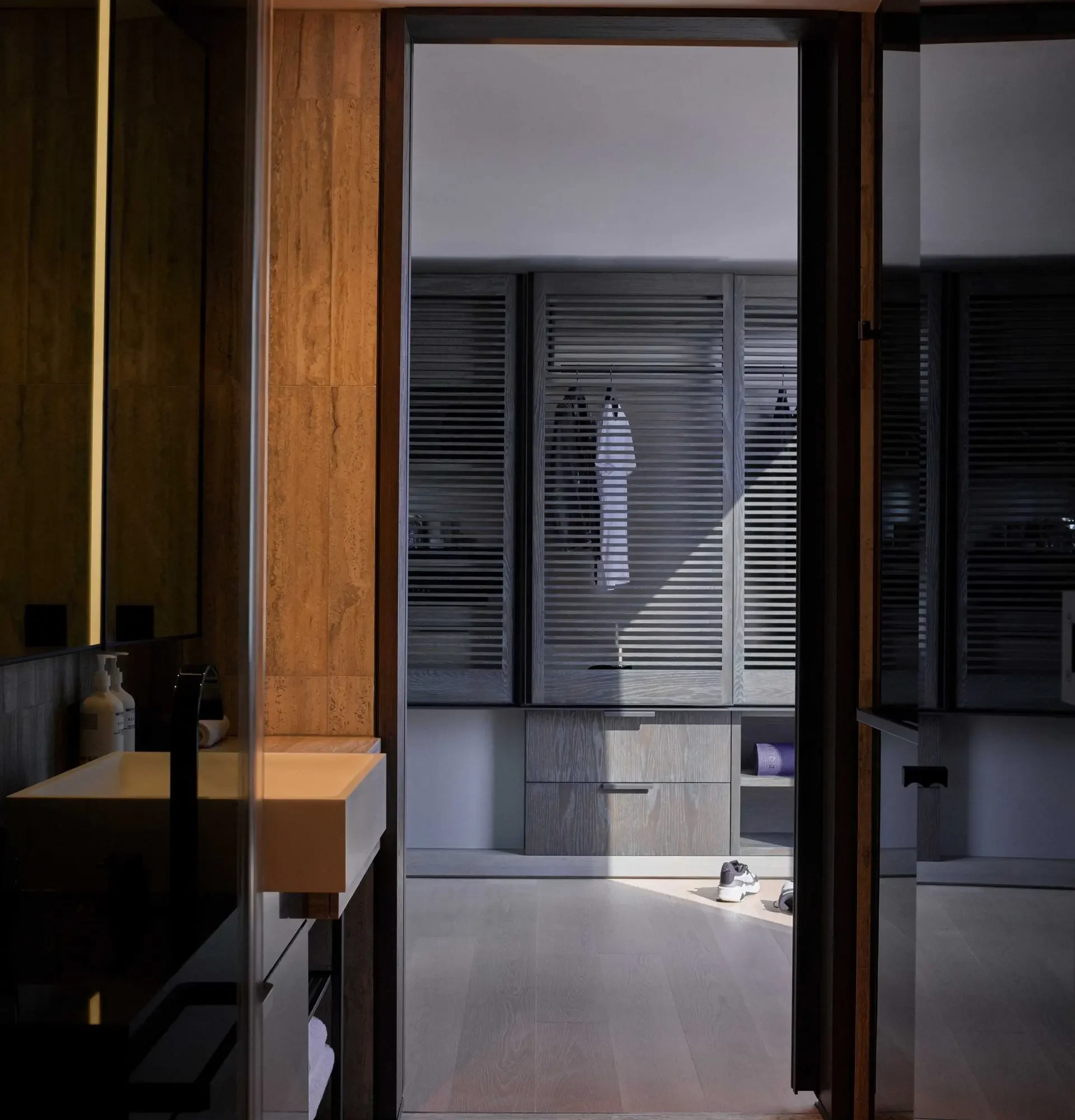 Modern Equinox hotel bathroom with sleek sink, dark wood panels, and view into sunlit walk-in closet