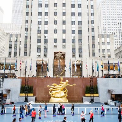 Rockefeller Center ice rink with Prometheus statue, international flags, and skaters in front of plaza facade