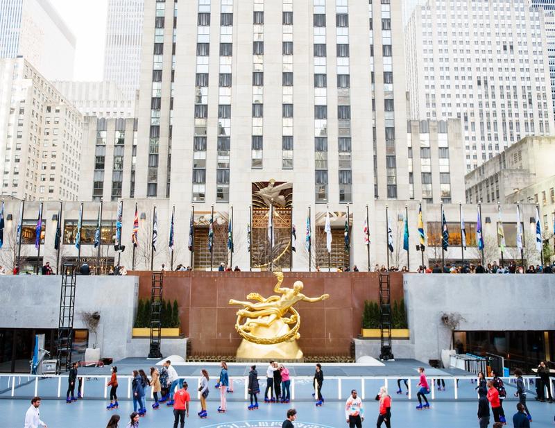 Rockefeller Center ice rink with Prometheus statue, international flags, and skaters in front of plaza facade