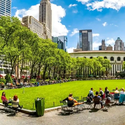 Bryant Park on sunny day with people relaxing on lawn and chairs, surrounded by trees and skyscrapers