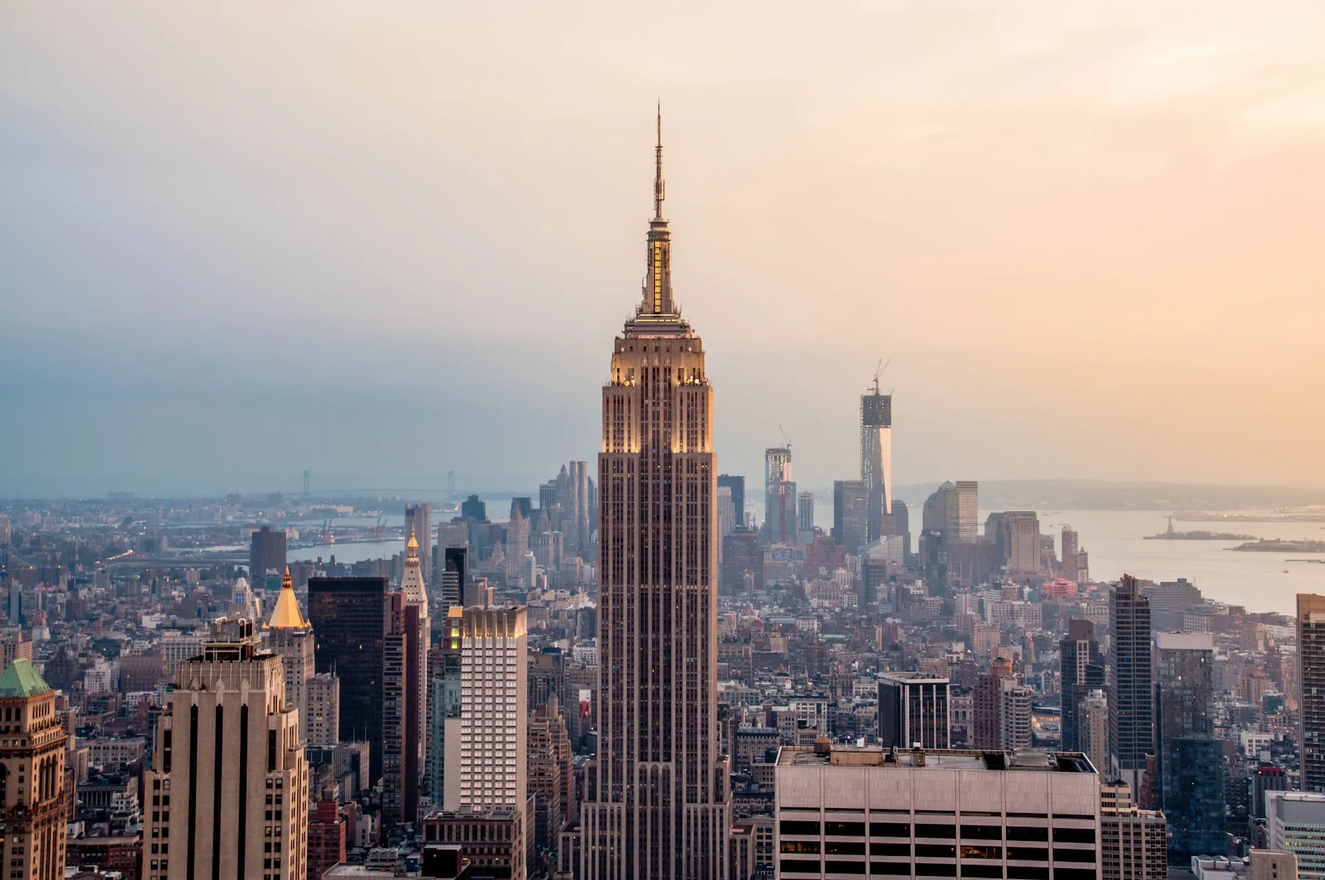 Empire State Building centered in Manhattan skyline at sunset with warm light and distant Hudson River