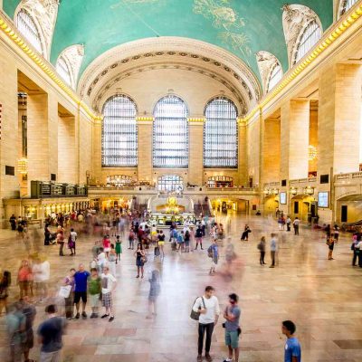 Grand Central Terminal main concourse with turquoise constellation ceiling, American flag, and bustling crowd