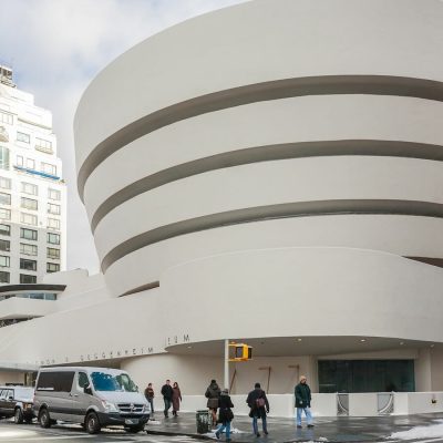 Guggenheim Museum exterior with spiral white facade, street traffic, and pedestrians in urban New York setting