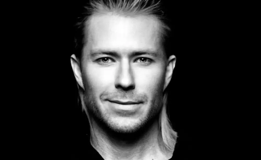 Black-and-white portrait of a man with short spiked hair against a dark background.