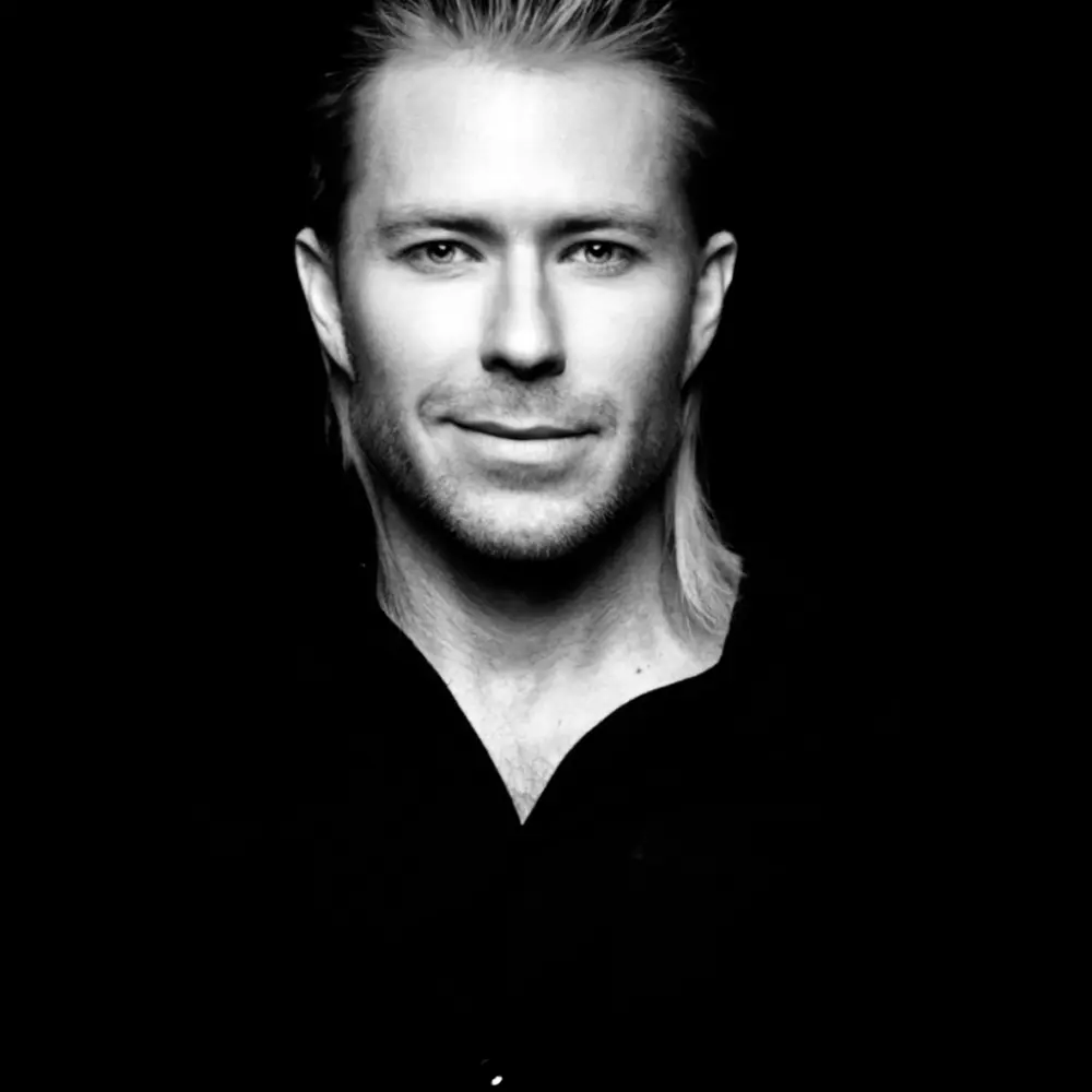 Black-and-white portrait of a man with slicked-back hair against a dark background.
