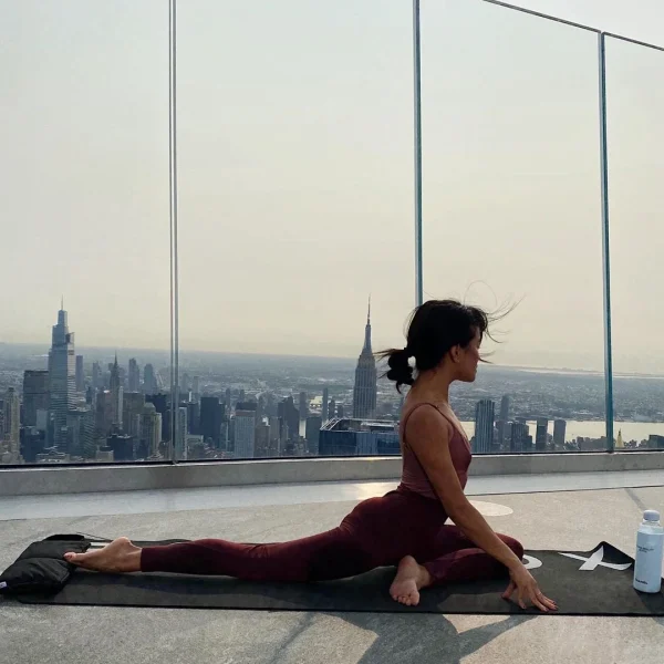 Woman practicing pigeon yoga pose on the edge of an observation deck at Equinox Hotel New York, with sweeping views of the Empire State Building and iconic NYC skyline at golden hour, blending mindfulness, motion, and urban energy.