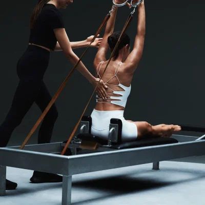 Individual performing Pilates on reformer machine with instructor guidance, set in minimalist studio, evoking precision, alignment, and elevated training