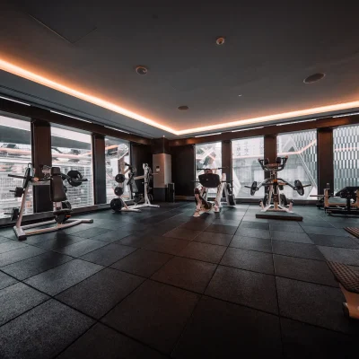 Modern indoor gym with strength training equipment, dark flooring, and floor-to-ceiling windows, evoking elevated fitness and sleek urban design
