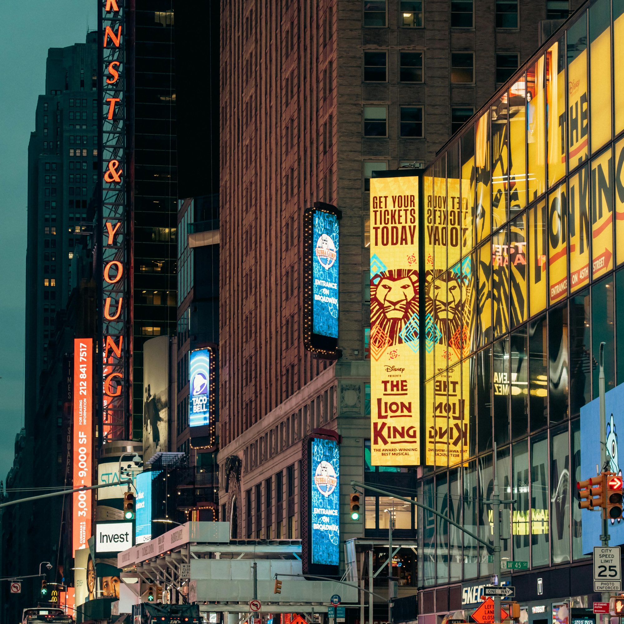 Broadway Theater District street view at dusk with “The Lion King” marquee, city traffic, and illuminated Midtown buildings
