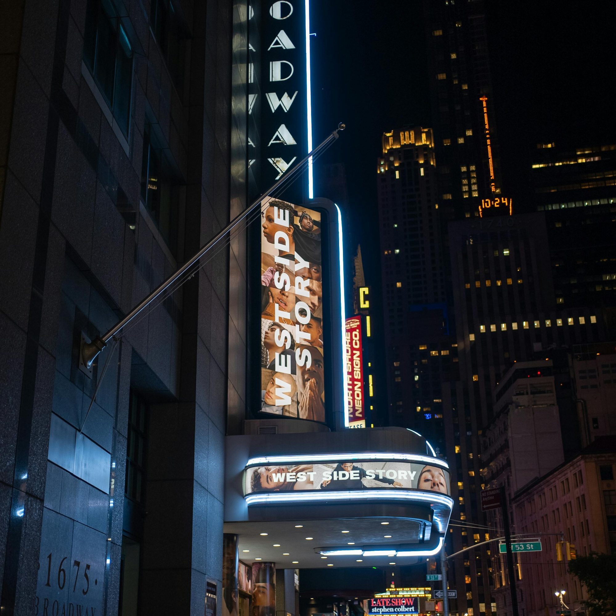 Broadway theater marquee at night in Midtown Manhattan featuring “West Side Story,” with neon signage and city skyline in the background