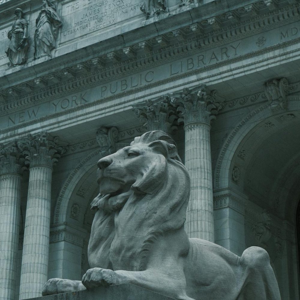 Close-up view of the New York Public Library’s stone facade, featuring carved statues and engraved text honoring the Astor Library above ornate architectural detailing.