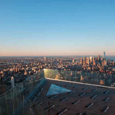 Panoramic cityscape from Edge observation deck with glass floor and directional panels, evoking architectural vastness and sunrise clarity