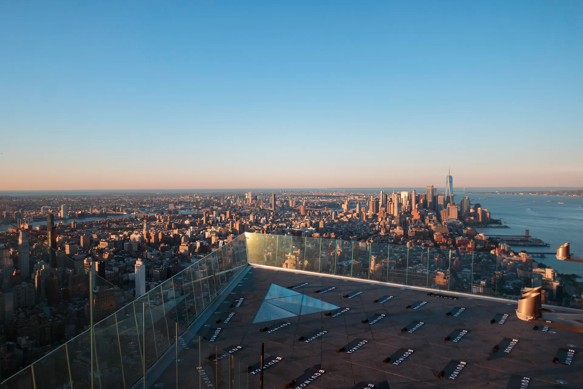 Panoramic cityscape from Edge observation deck with glass floor and directional panels, evoking architectural vastness and sunrise clarity