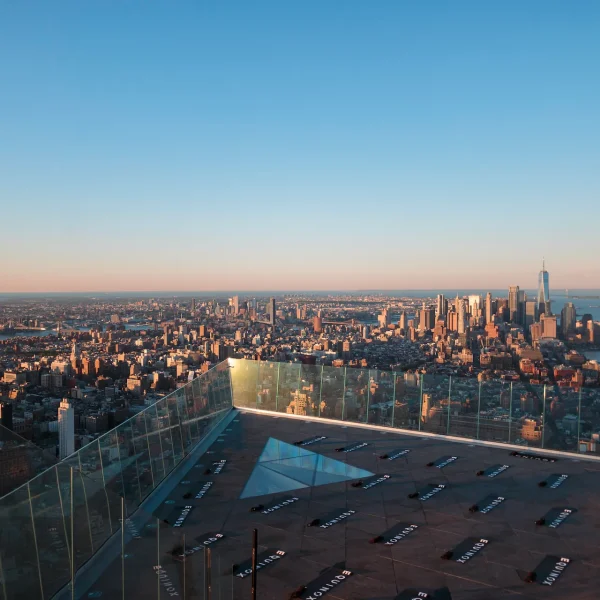 Panoramic cityscape from Edge observation deck with glass floor and directional panels, evoking architectural vastness and sunrise clarity