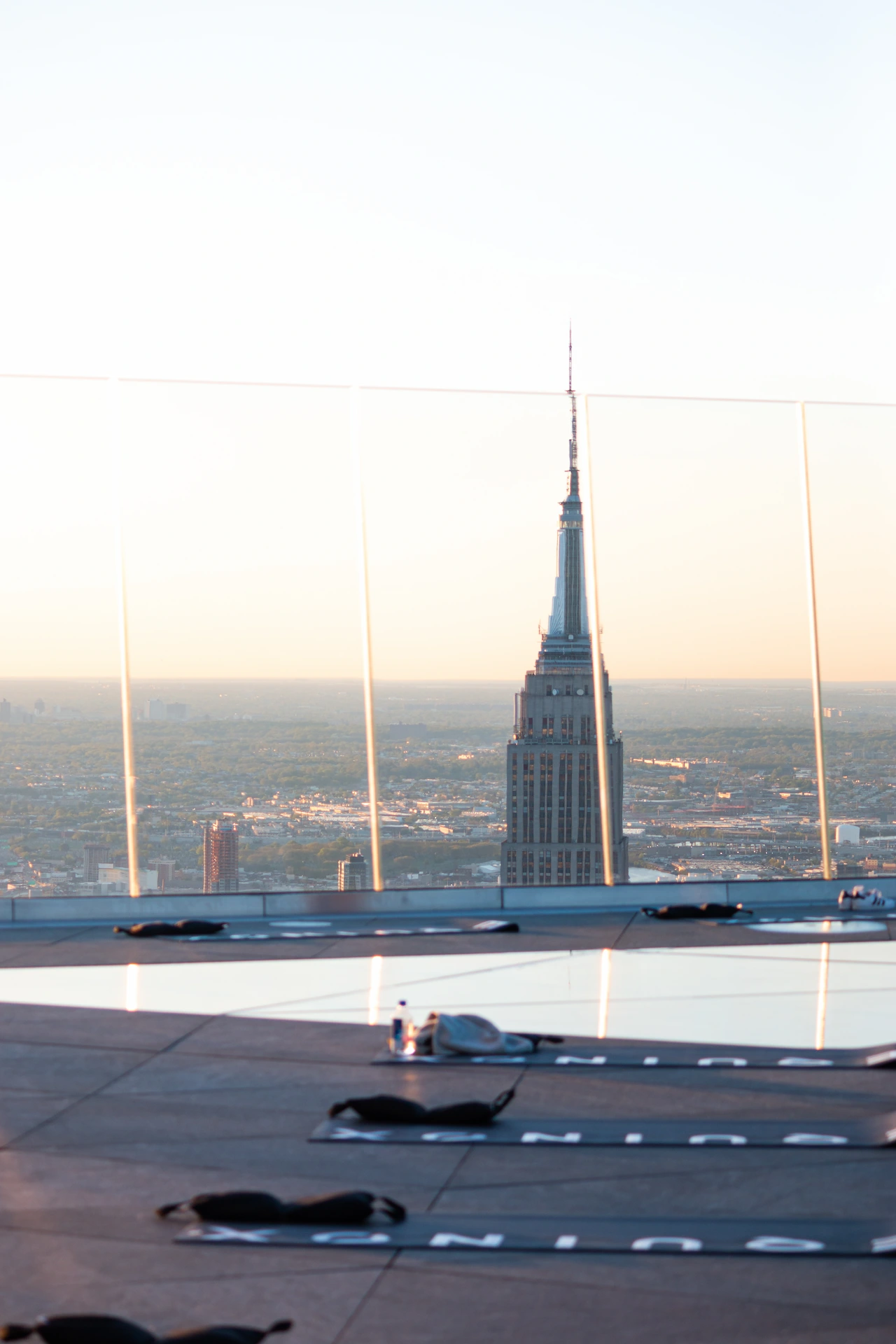 Rooftop yoga setup with Empire State Building in view, reflective flooring and warm light, evoking urban stillness and elevated perspective